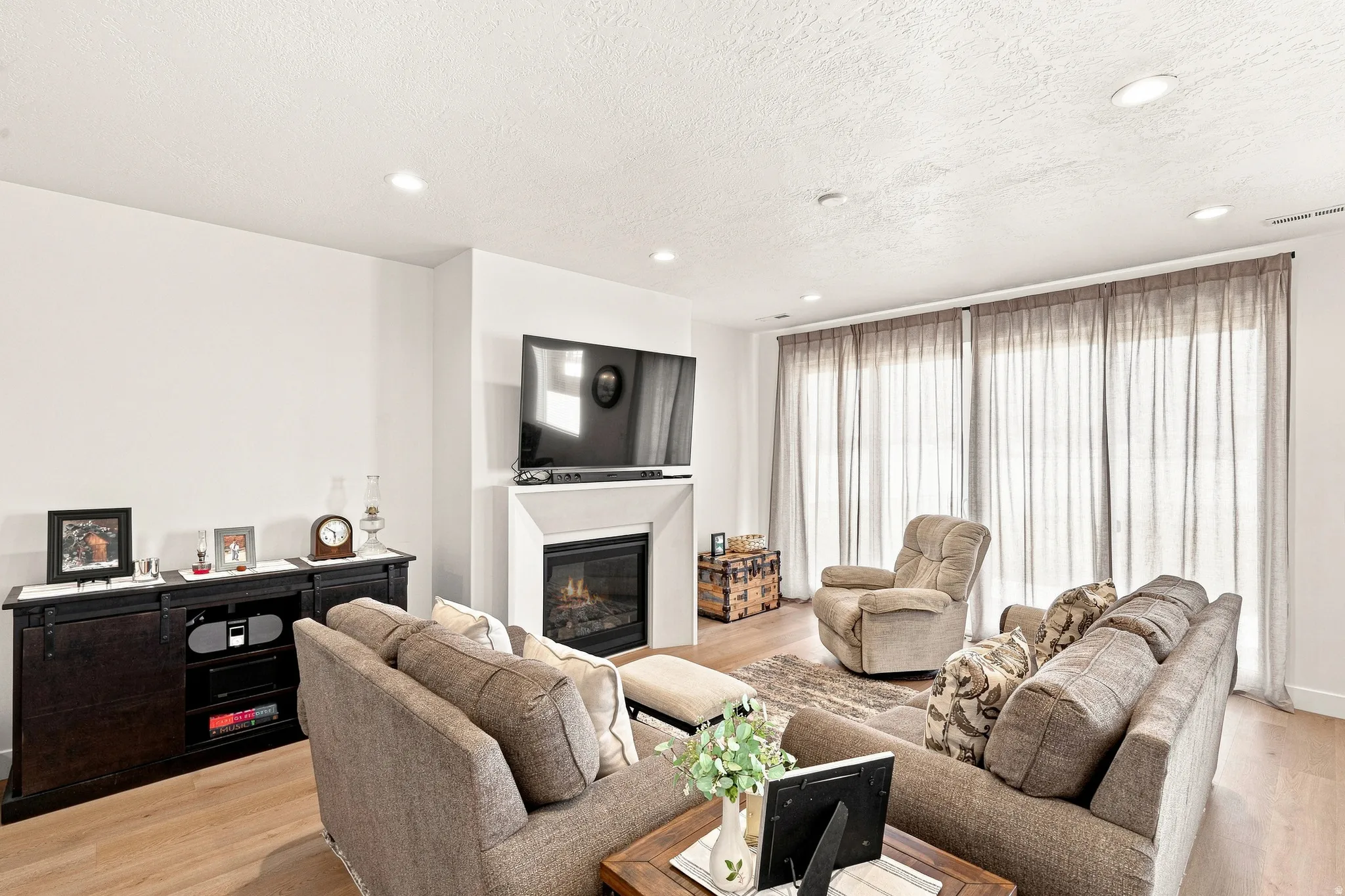 Bright, open living area featuring a gas fireplace with built-in cabinetry, recessed ceiling lighting, and wood-finish flooring throughout