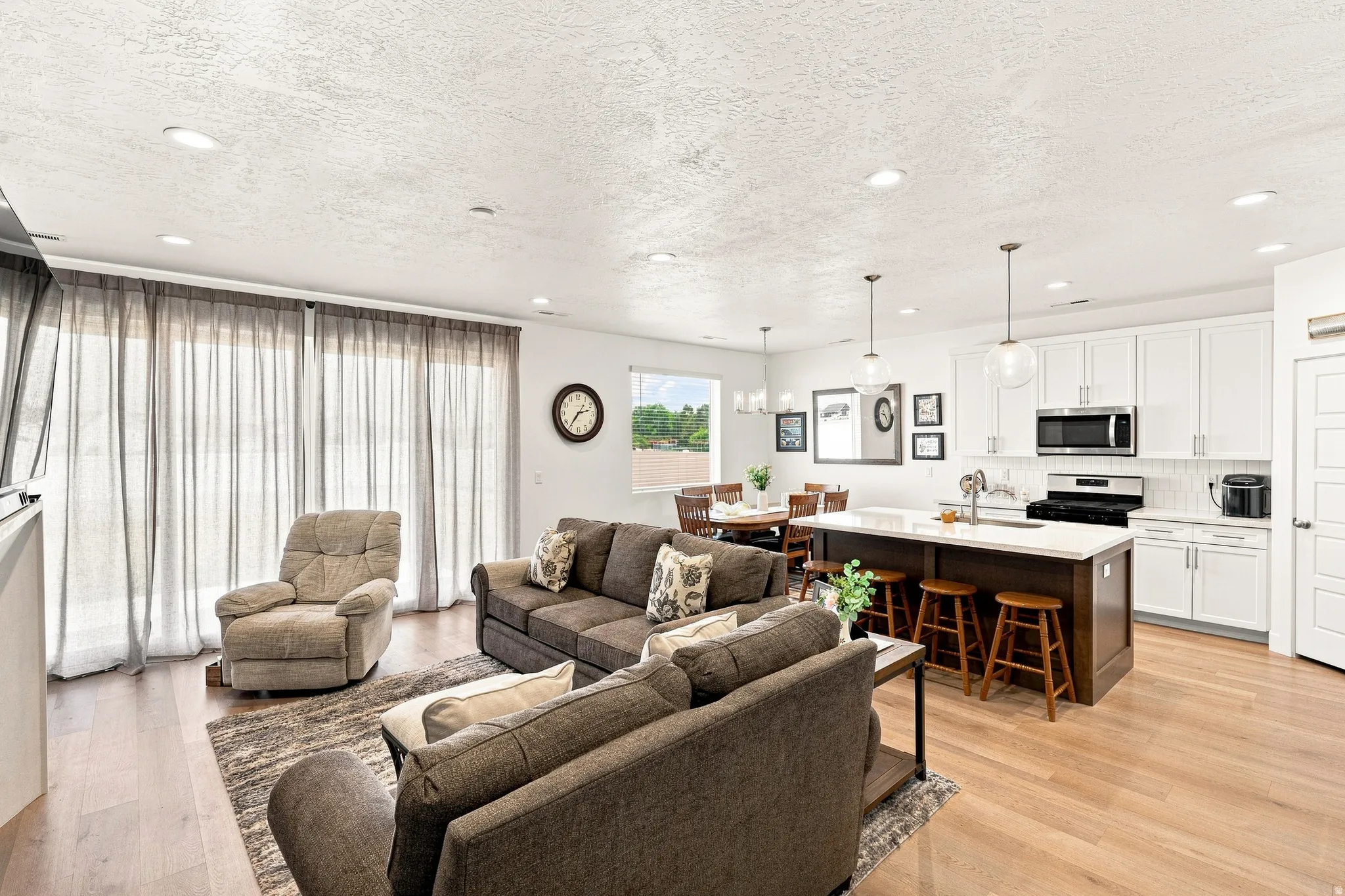 Open-concept living area featuring wood-finish flooring, recessed lighting, a kitchen island with seating, white cabinetry, and stainless-steel appliances