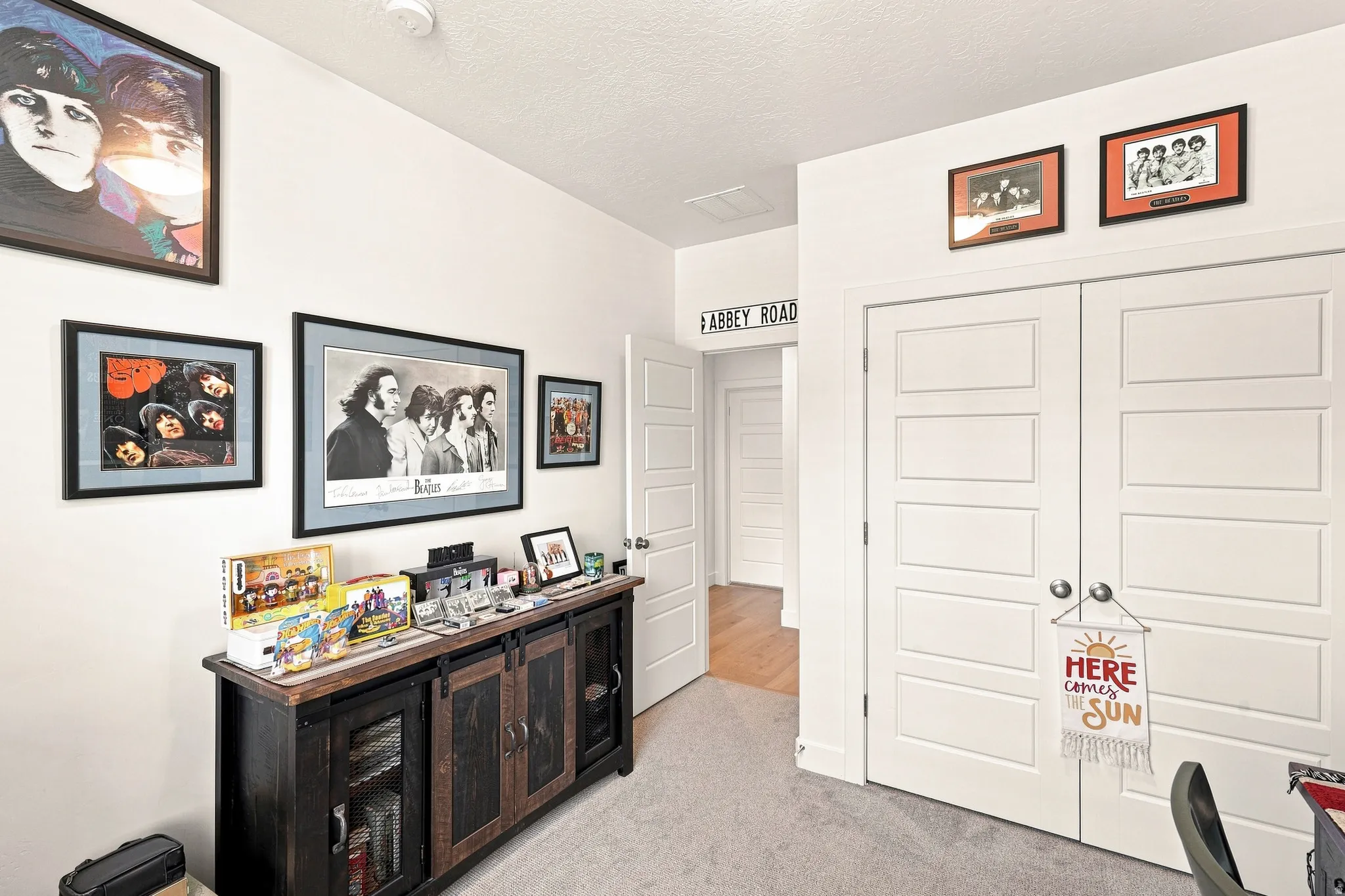 Dedicated media room featuring recessed ceiling lighting, dark wood-finish cabinetry with glass-front display storage, framed artwork throughout, and dual white six-panel closet doors