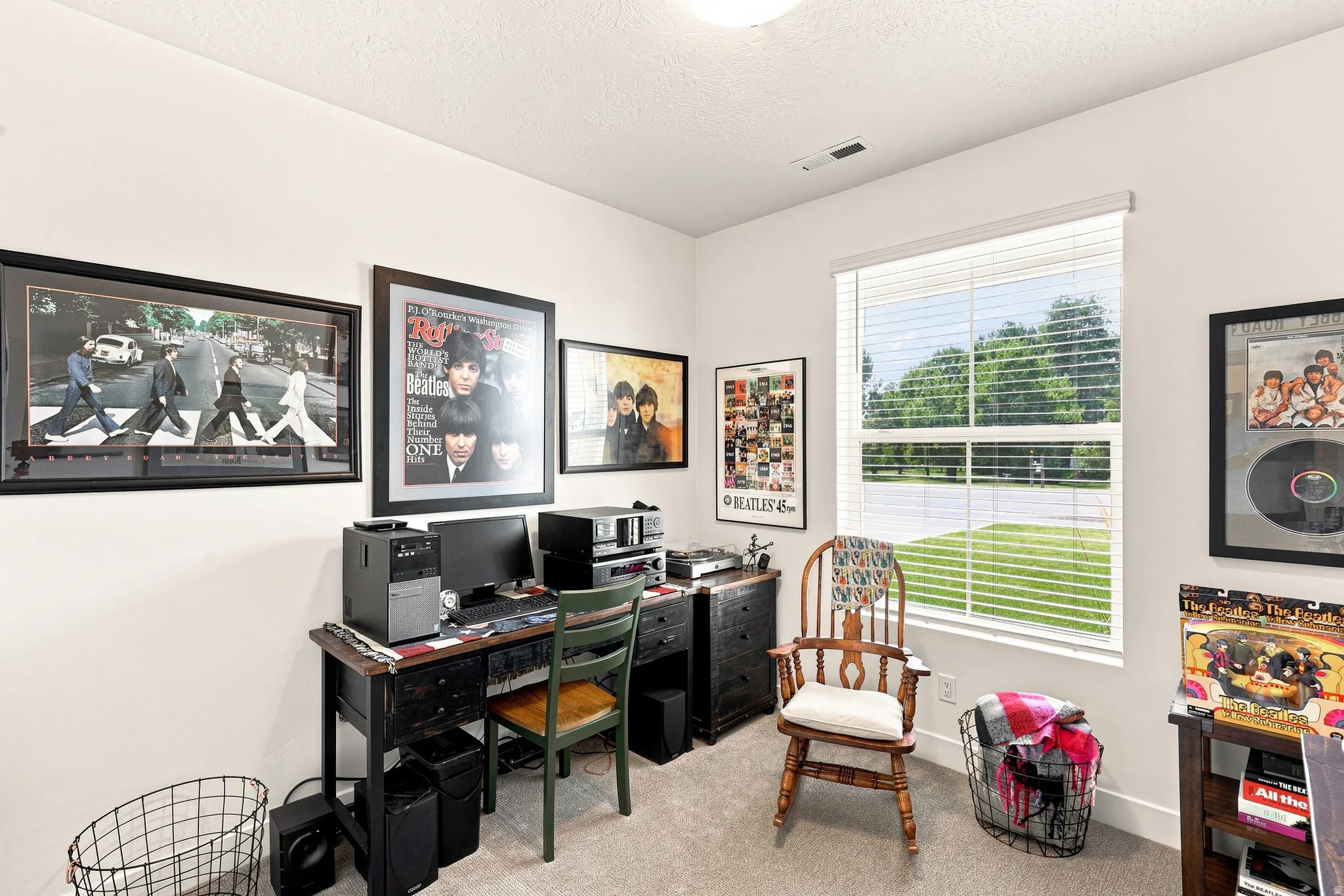 Dedicated home office featuring large windows with natural light, built-in desk workspace with black laminate surface, black storage cabinetry, carpet flooring, and framed wall art
