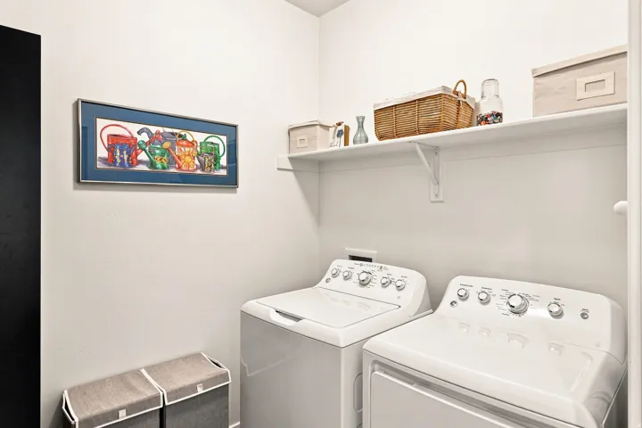 Dedicated laundry room featuring side-by-side washer and dryer with full-size capacity, open shelving with woven storage baskets, and bright white finishes throughout