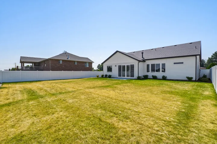 Spacious backyard featuring a white vinyl privacy fence, a newly constructed white exterior, a dark asphalt shingle roof, and a multi-panel sliding glass door