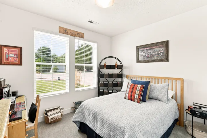 Bright secondary bedroom featuring large dual-pane windows with plantation shutters, wood-finish flooring, and ample natural light