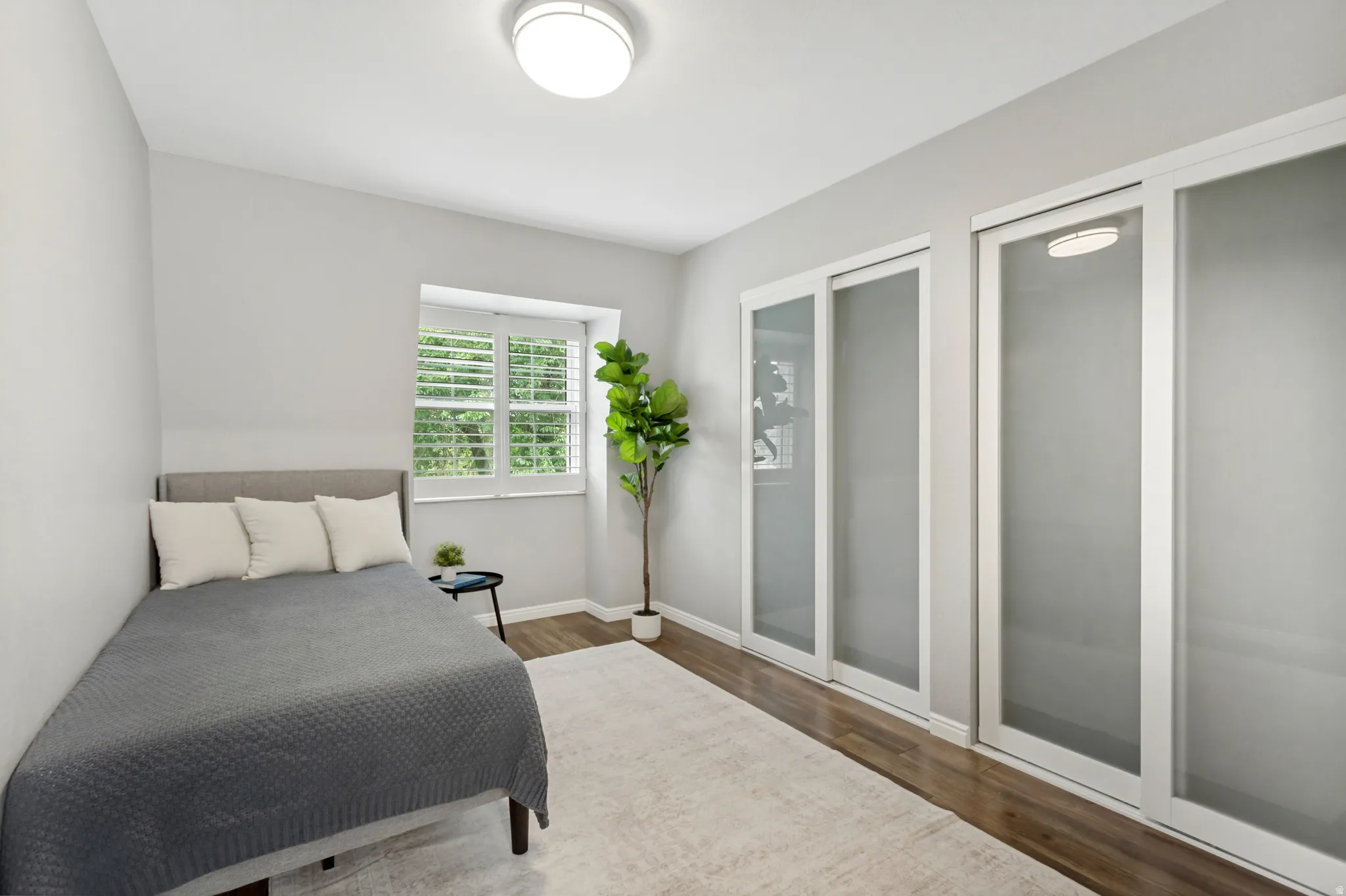 Bright secondary bedroom featuring abundant natural light from multi-pane windows, wood-finish flooring, neutral wall finishes, and direct access to a spacious closet system with beautiful sliding doors