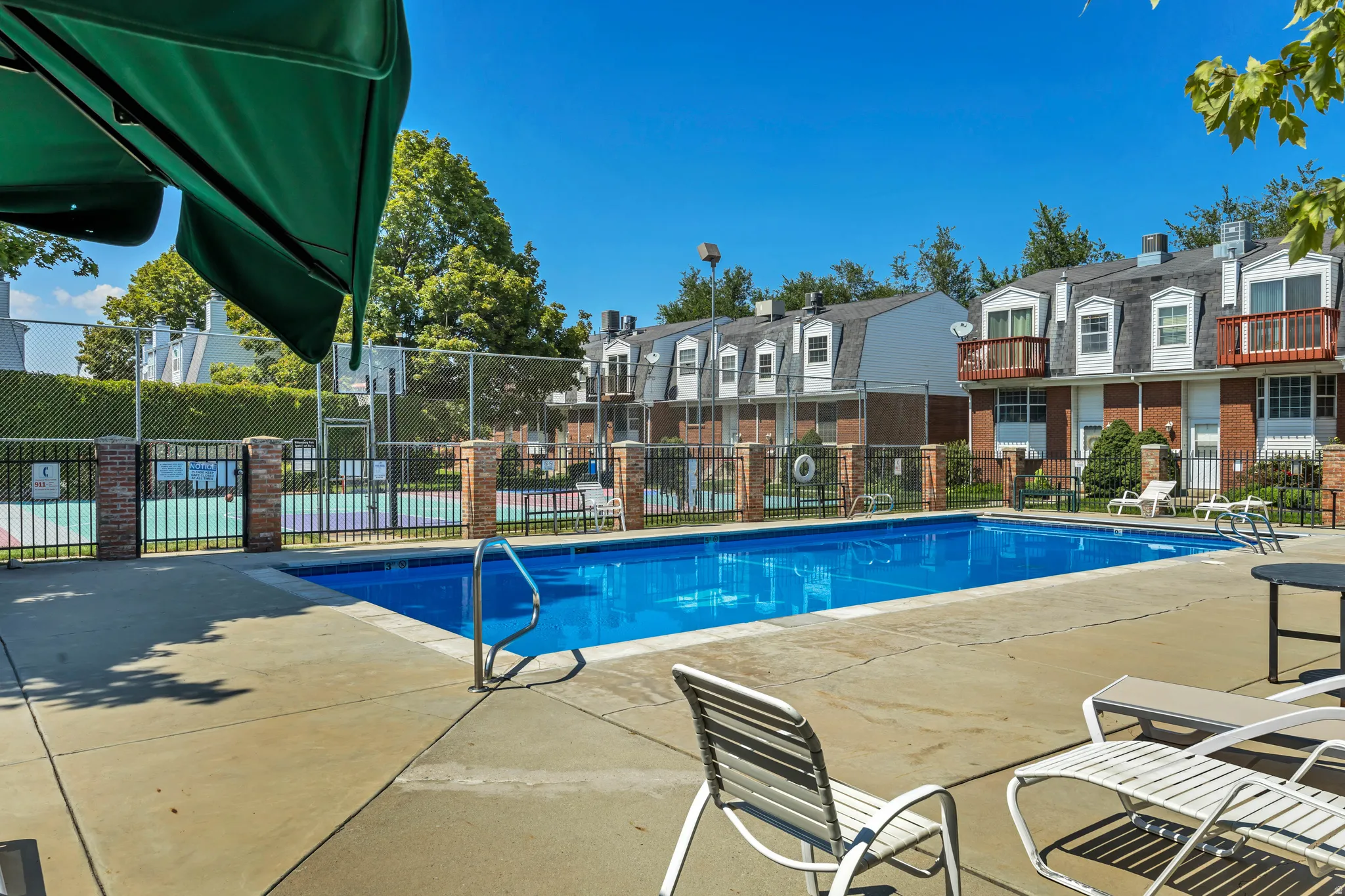 Swimming pool with concrete surround, surrounded by a metal fence with brick pillars