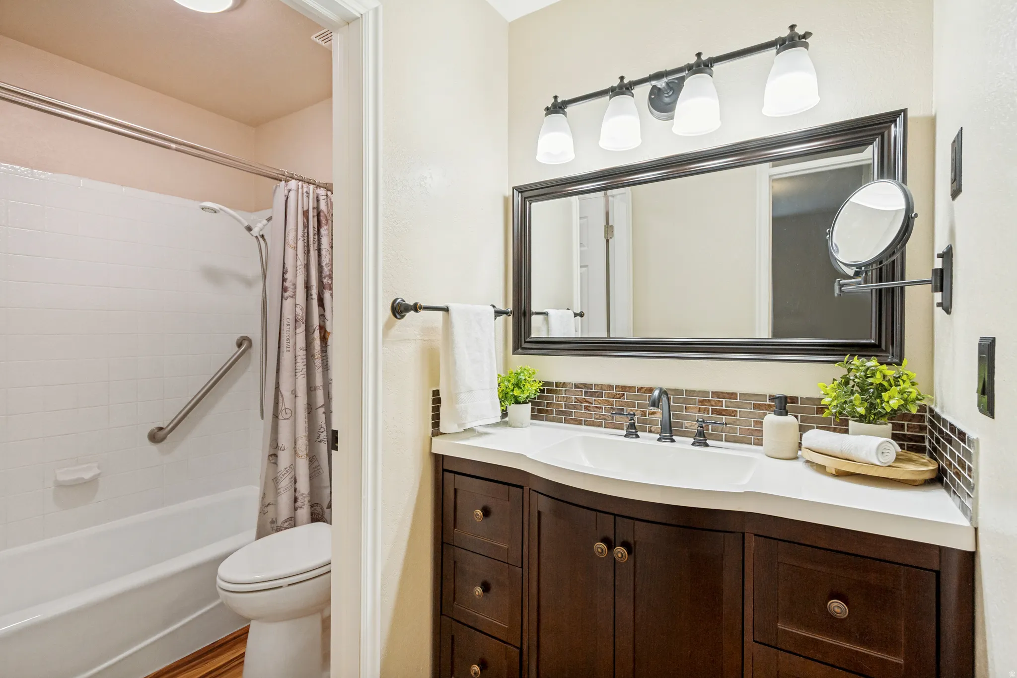Bathroom featuring a white bathtub with a grab bar, wood-finish flooring, a dark wood-finish vanity with a white countertop, a rectangular undermount sink, and a framed mirror with overhead lighting