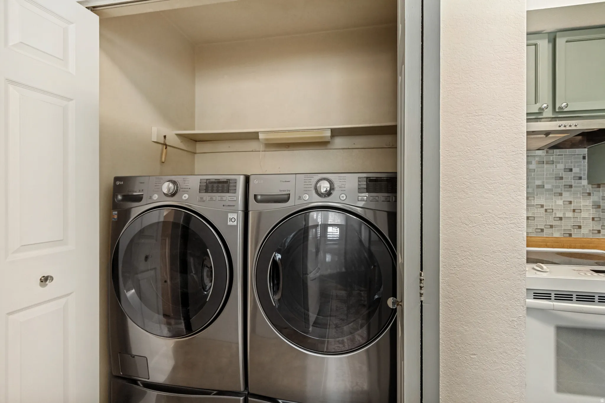 Dedicated laundryarea featuring side-by-side front-load washers and dryers with stainless steel finishes, built-in shelving above for storage,