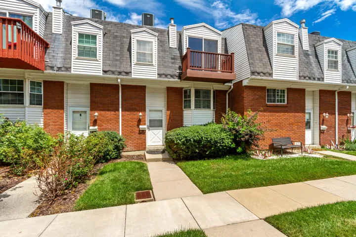 Brick townhome with mansard roofline featuring dormer windows, white and brick exterior finishes, and individual front entrance with concrete walkway