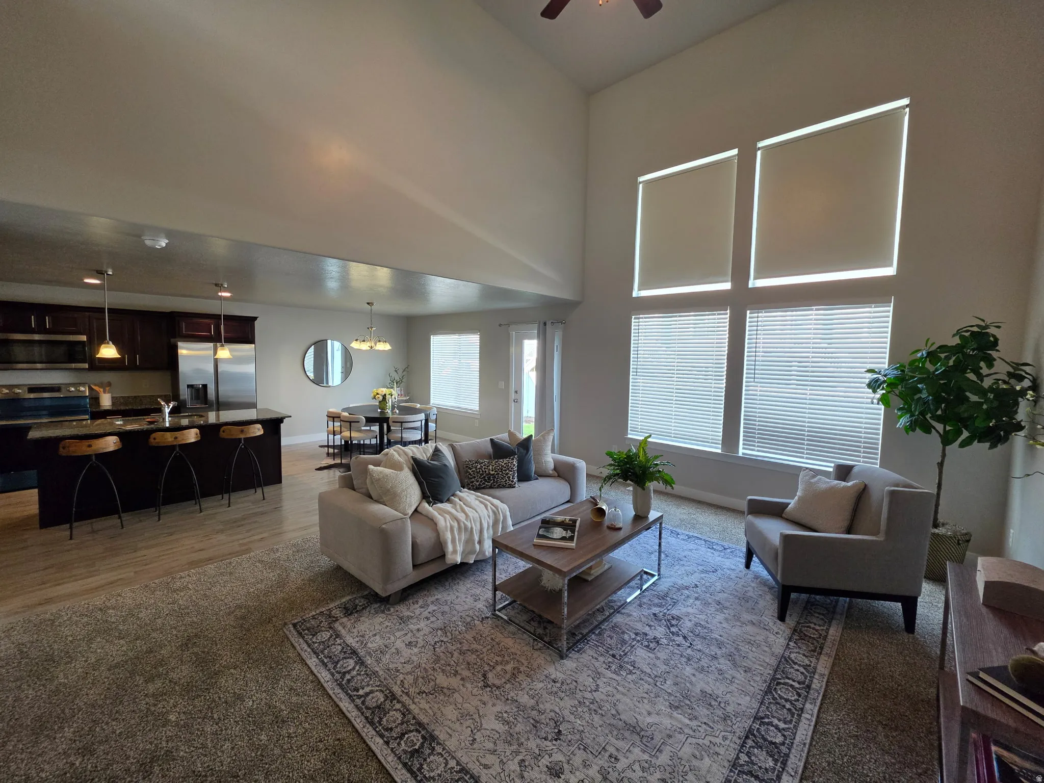 Open-concept living space featuring soaring ceilings with ceiling fan, expansive windows with motorized blinds flooding the area with natural light, wood-finish flooring throughout, and a thoughtfully designed layout that combines the living room, dining