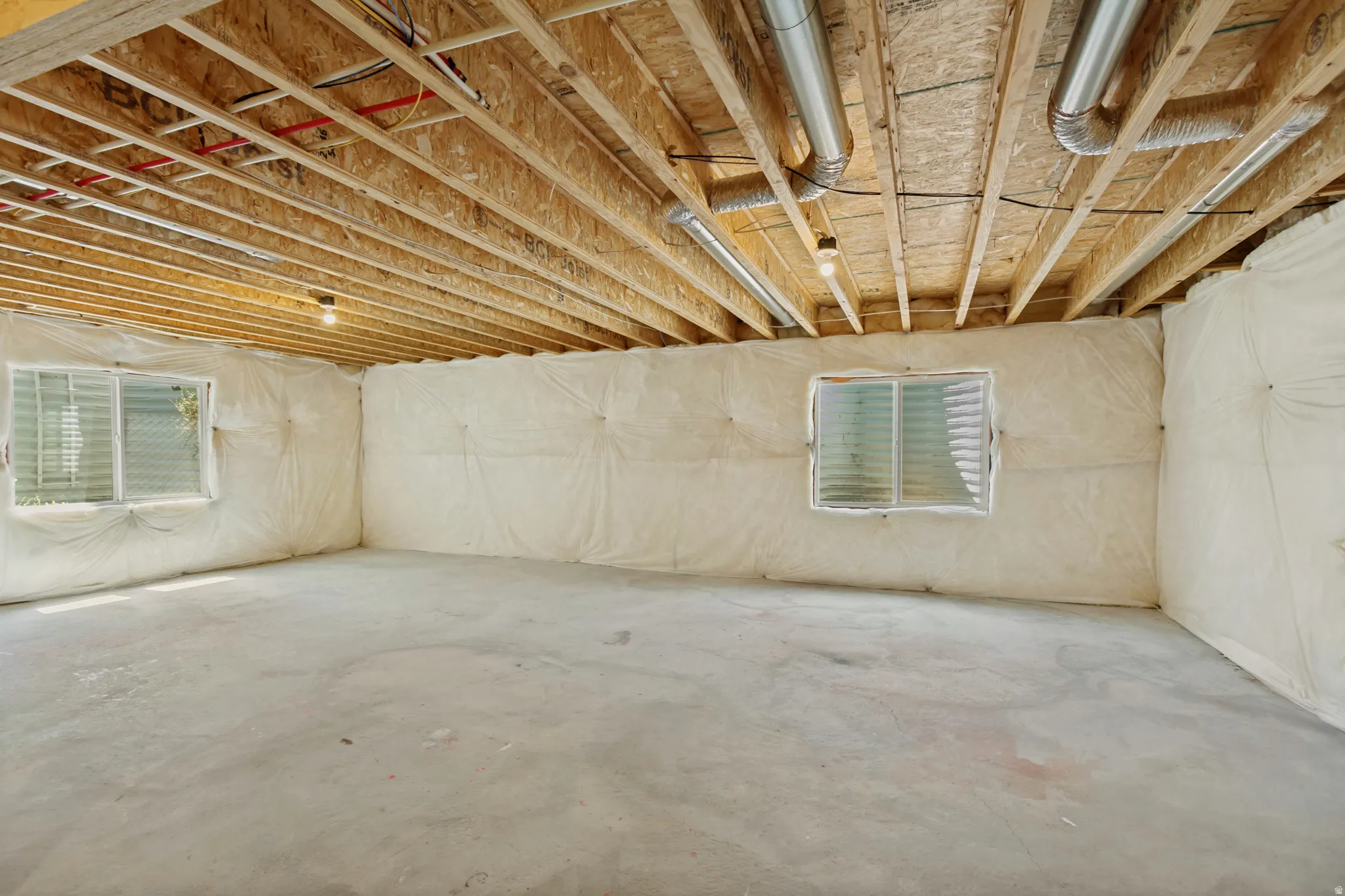 Unfinished basement with exposed ceiling joists, concrete flooring, two egress windows, and insulated walls