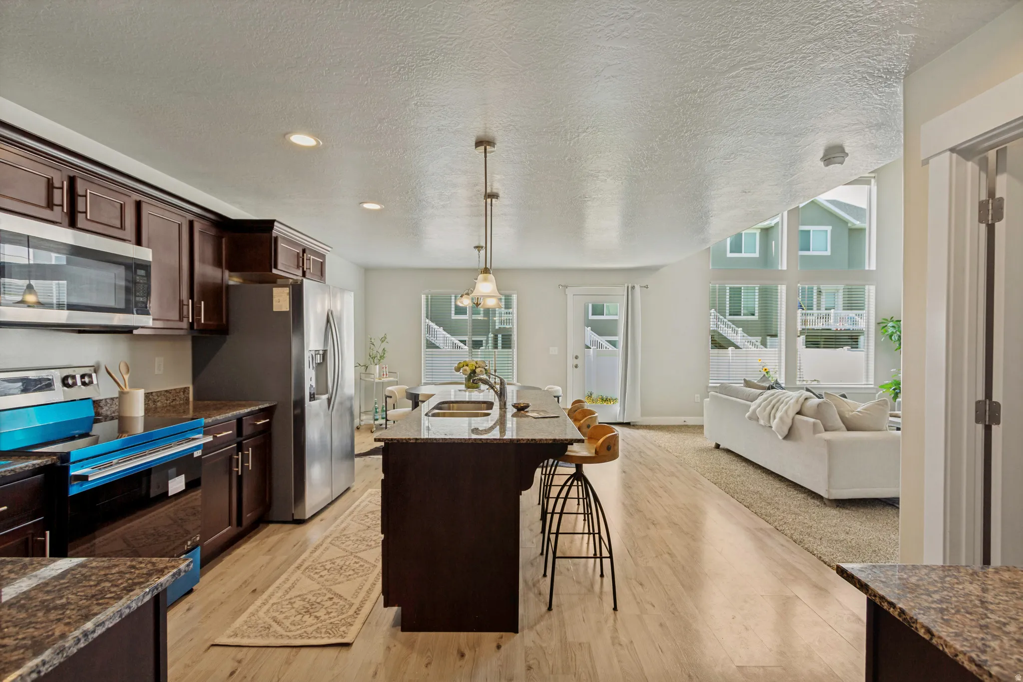 Open-concept living space with wood-finish flooring, kitchen island, and stainless steel appliances