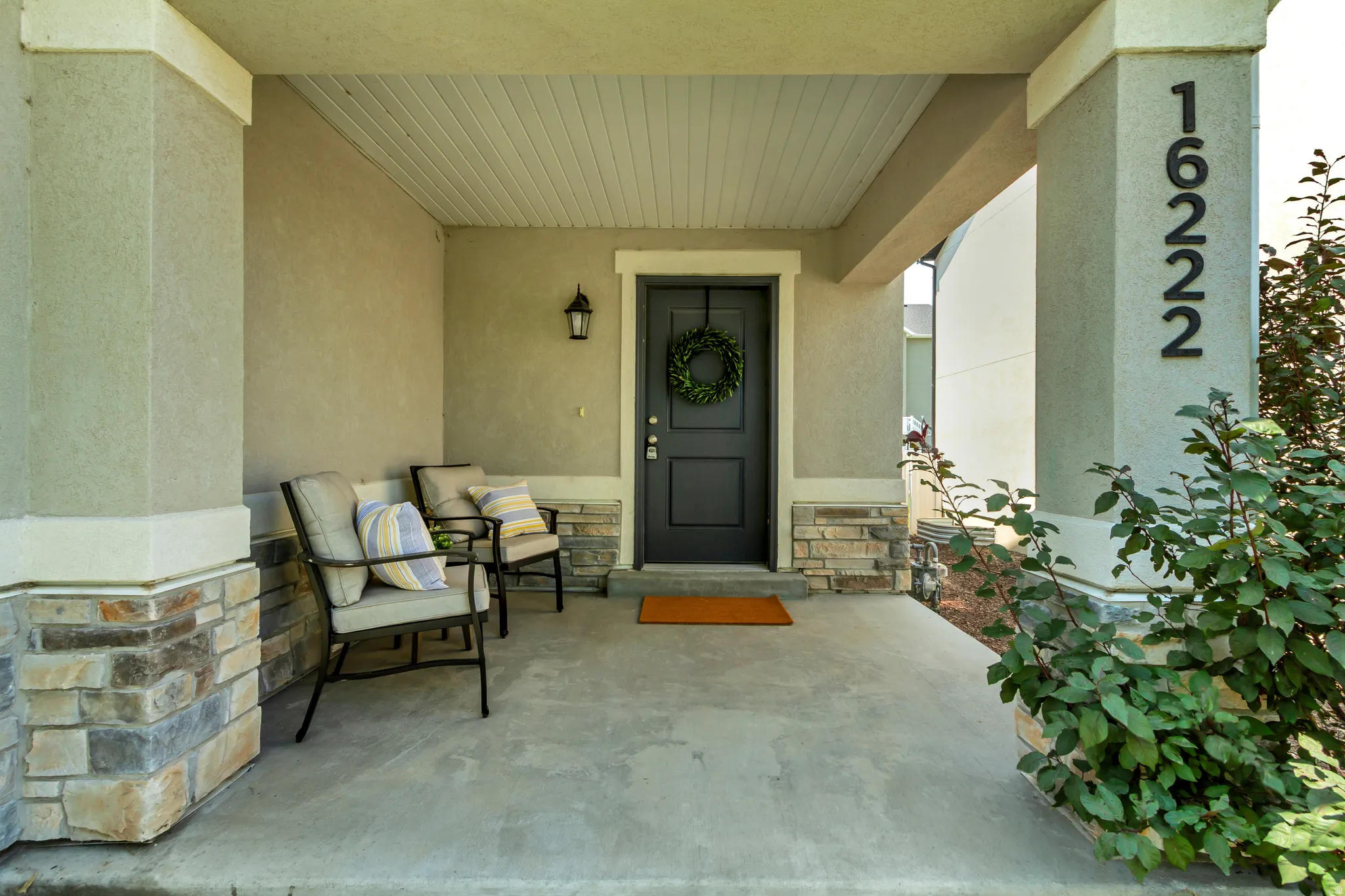 Inviting covered porch with a dark gray entry door, concrete flooring, stucco siding, and stone accents