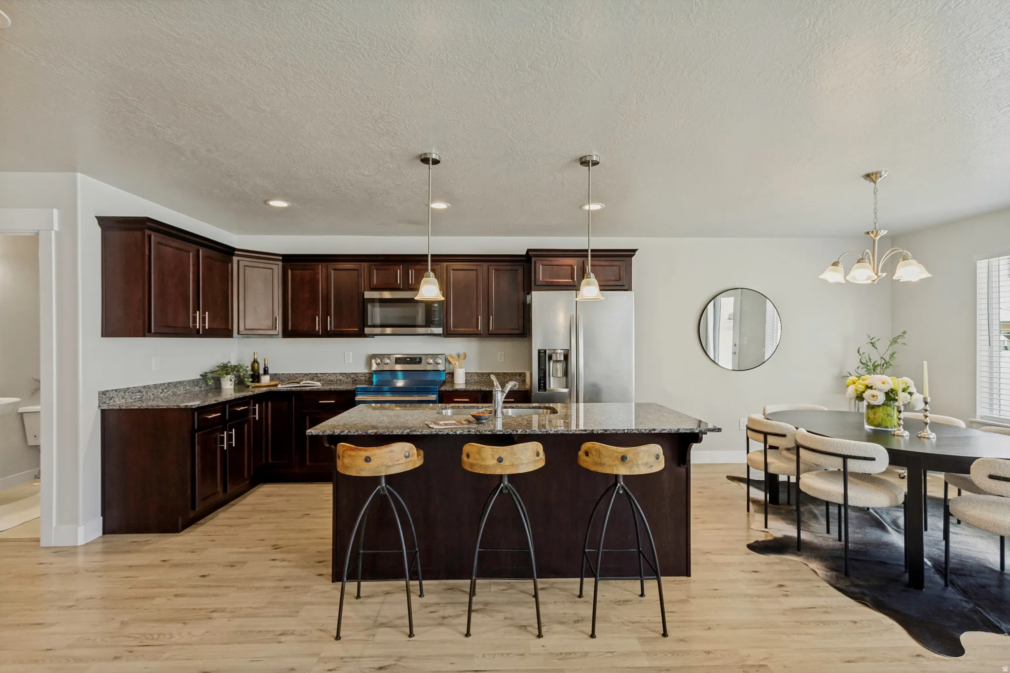 Kitchen featuring dark wood cabinetry, stainless steel appliances, a center island with pendant lighting, and light wood-finish flooring
