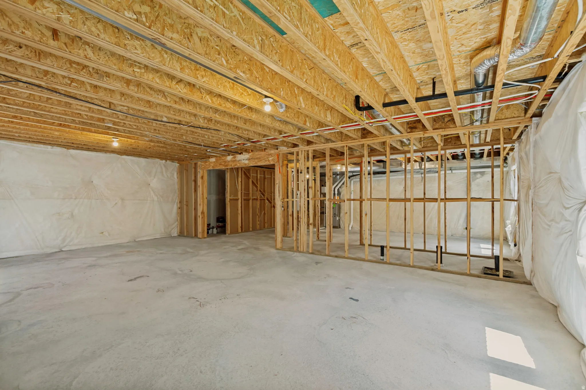 Unfinished basement with exposed ceiling joists, concrete flooring, framing for interior walls, and visible plumbing and ductwork