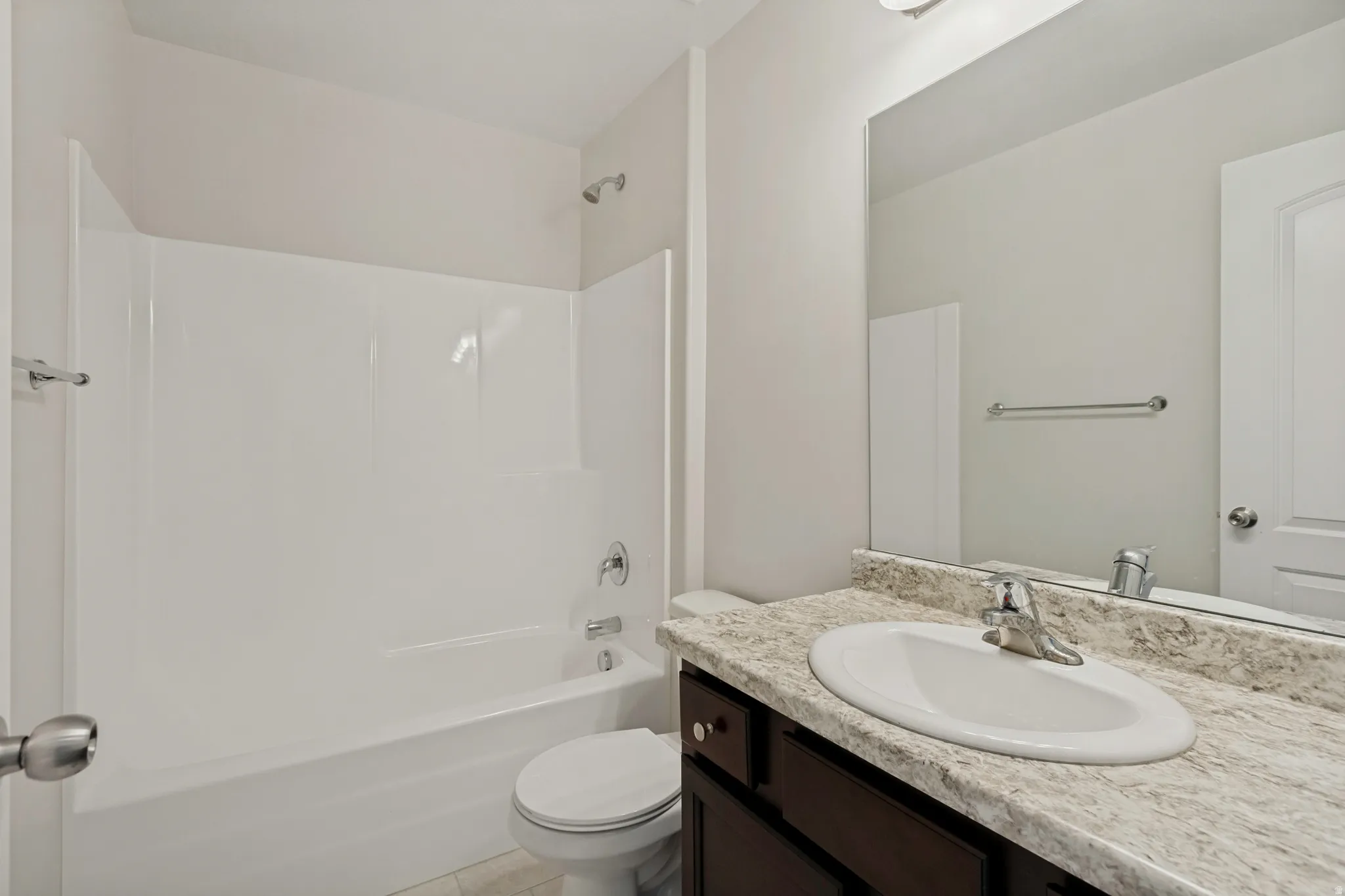 White integrated tub and shower unit, dark wood-finish vanity with an undermount sink, stone-finish countertop, and a large wall-mounted mirror