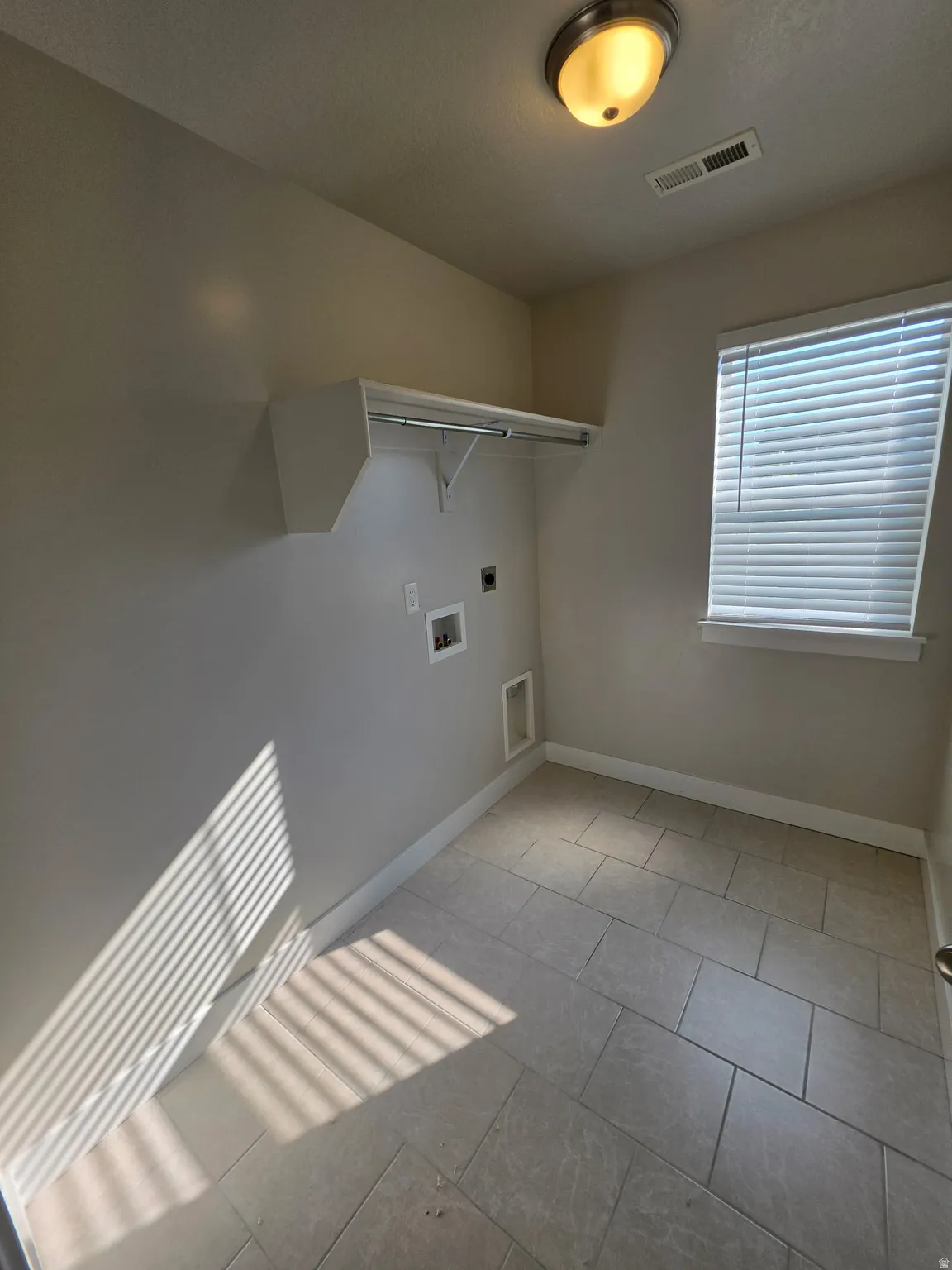 Utility room featuring a built-in shelf with hanging rod, a window with blinds, overhead lighting, and tiled flooring