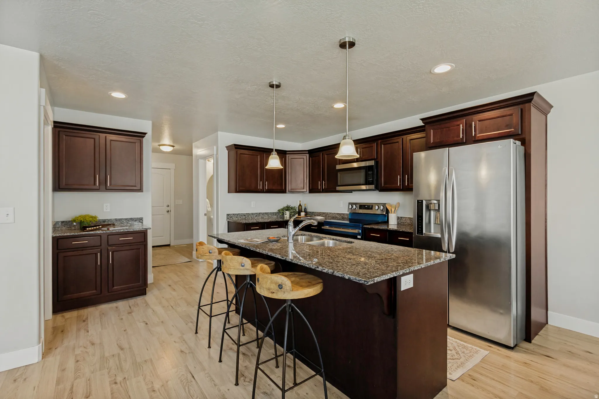Kitchen featuring dark wood cabinetry, stainless steel appliances, granite countertops, a central island, and wood-finish flooring