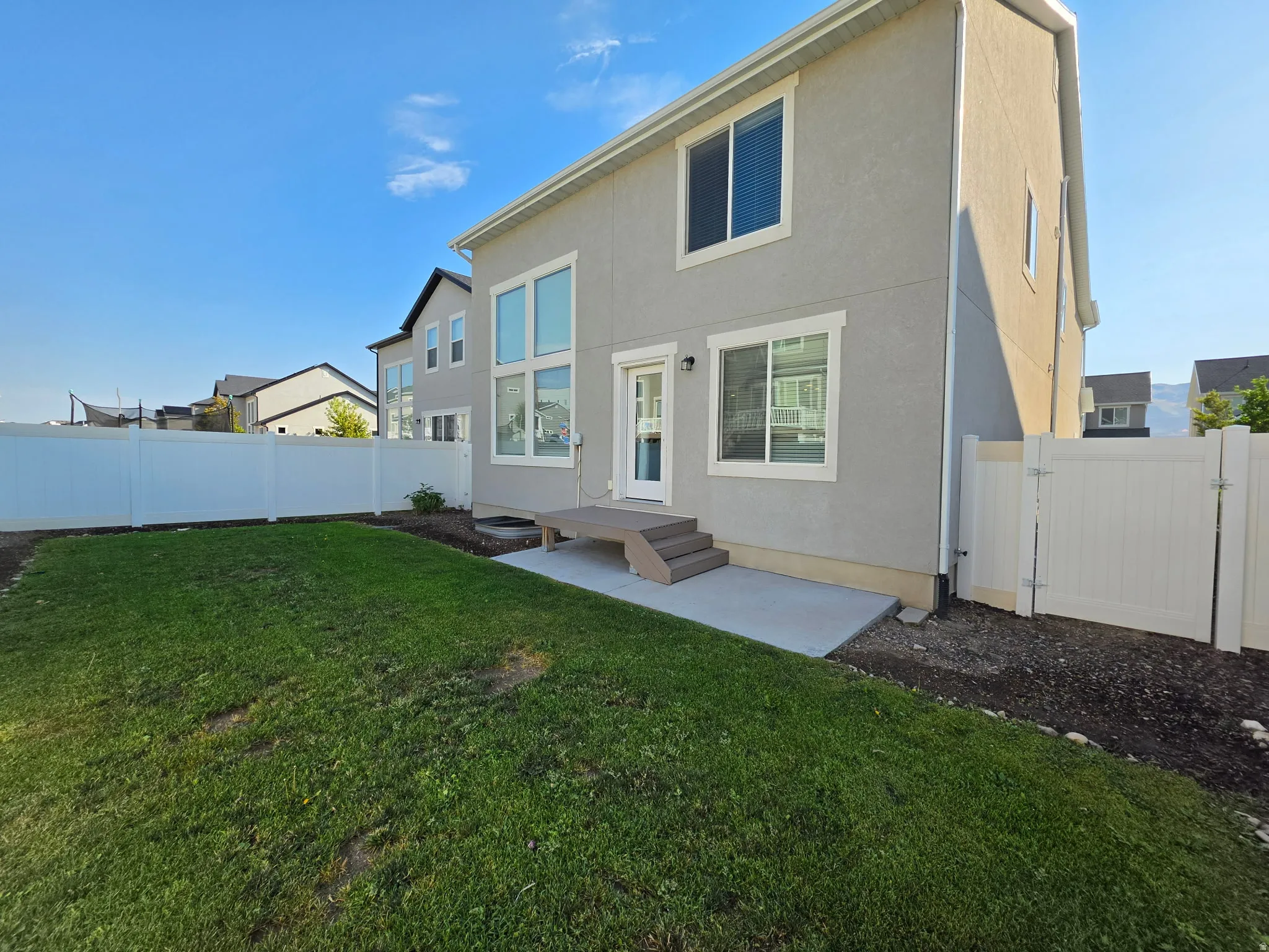 Modern home featuring a spacious rear exterior with manicured lawn, concrete patio, and white vinyl fencing