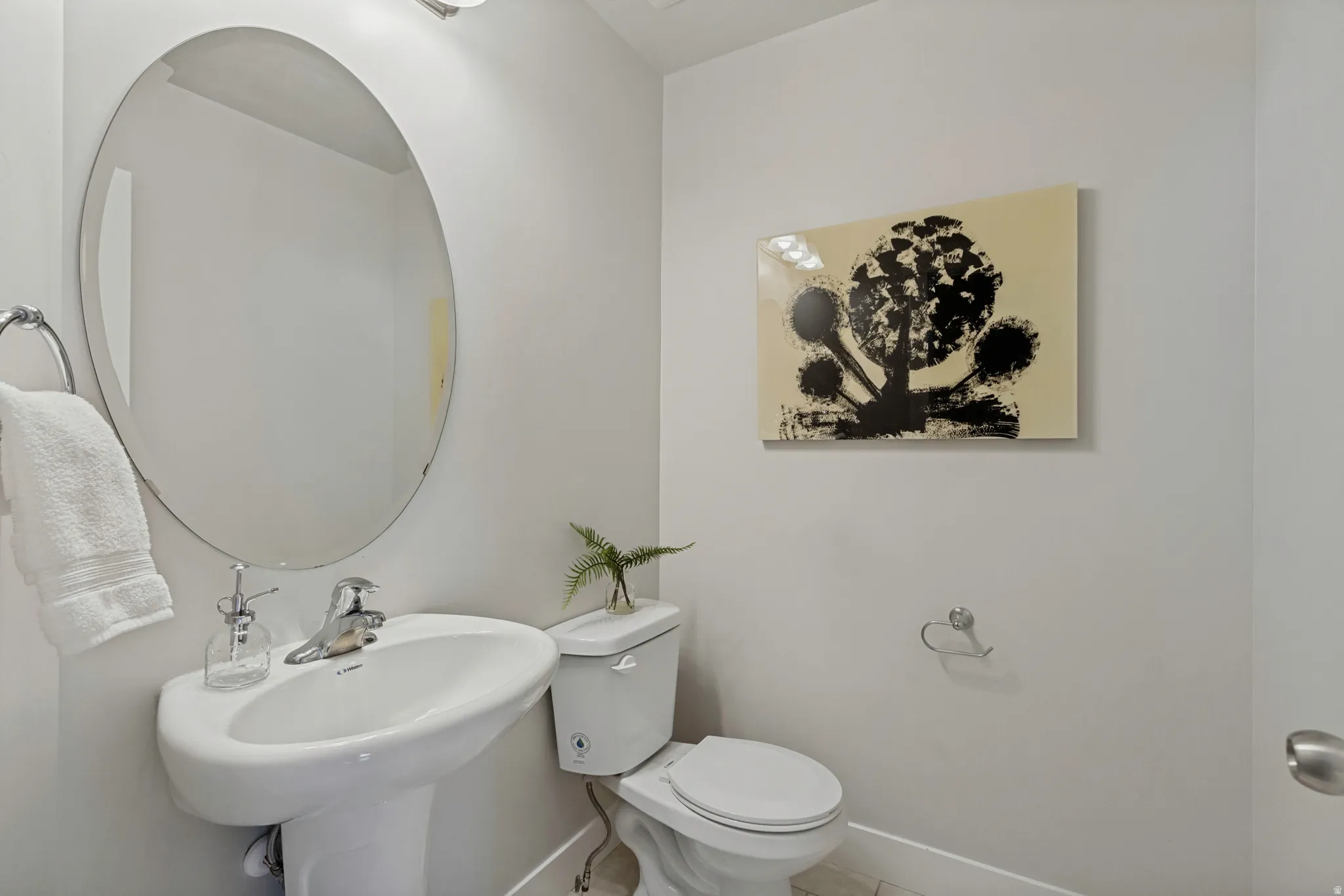 Pedestal sink with chrome faucet, oval wall mirror, and modern wall sconce