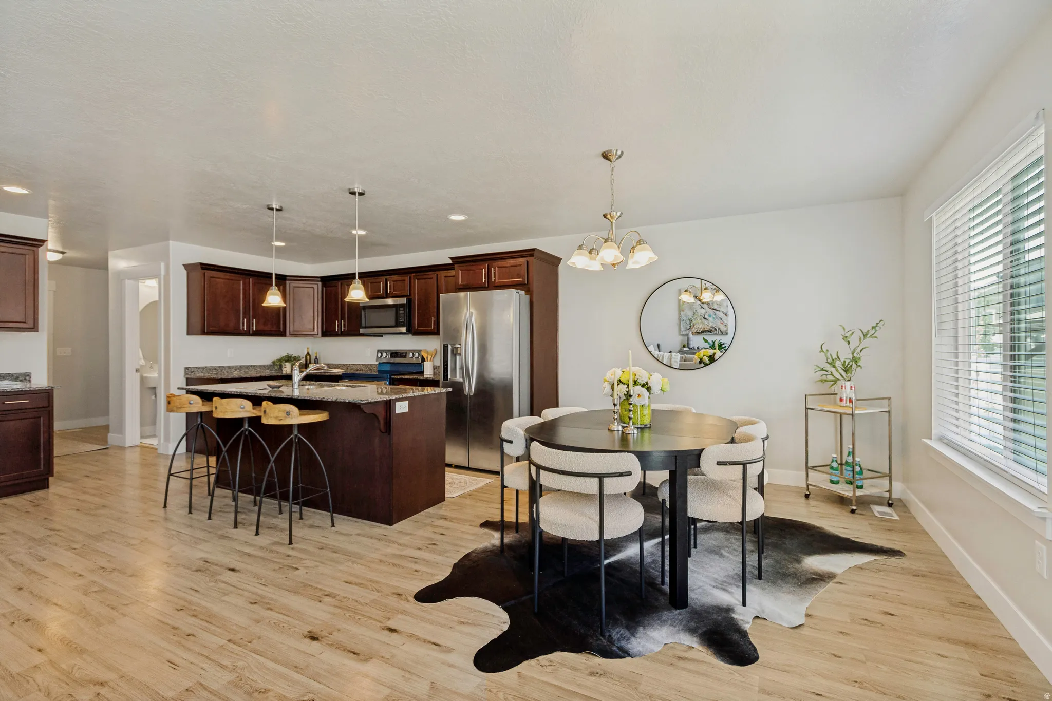 Open-concept living area featuring wood-finish flooring, a kitchen island with pendant lighting, dark wood cabinetry, and a dining space with a multi-light chandelier