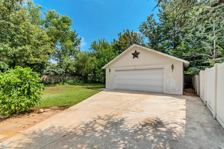 Spacious concrete driveway providing ample parking and vehicle access, leading to a detached garage featuring a white panel overhead door and decorative star accent