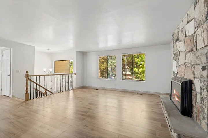 Stone-clad fireplace with hearth, wood-finish flooring, staircase with wood newel post and metal balusters, and transom windows