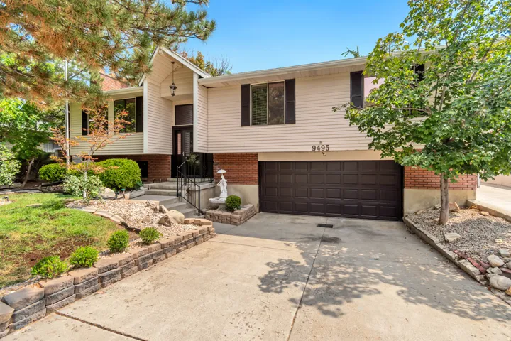 Split-level residence featuring a two-car garage, brick and siding exterior, concrete driveway, and mature landscaping