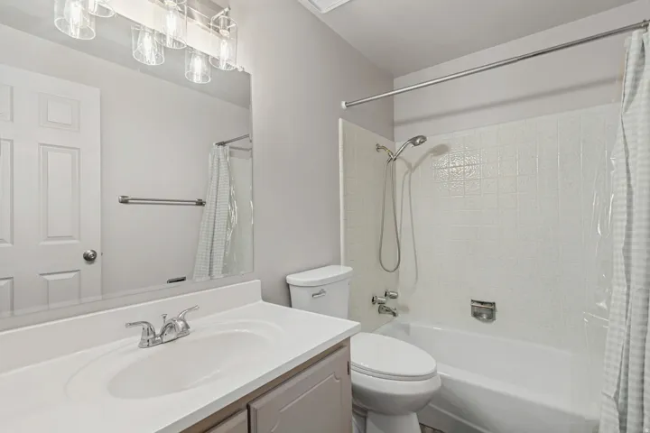 White tile tub and shower combination, vanity with integrated sink, and brushed nickel fixtures