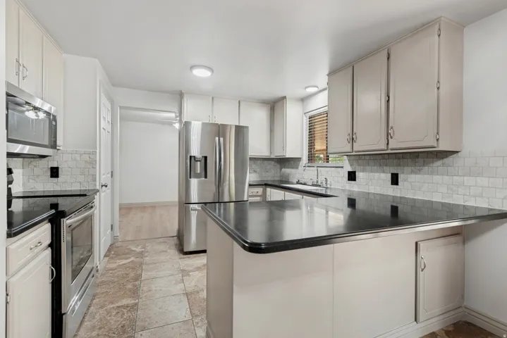 Kitchen featuring light-toned cabinetry, stainless steel appliances, dark countertops, a tiled backsplash, and tile flooring
