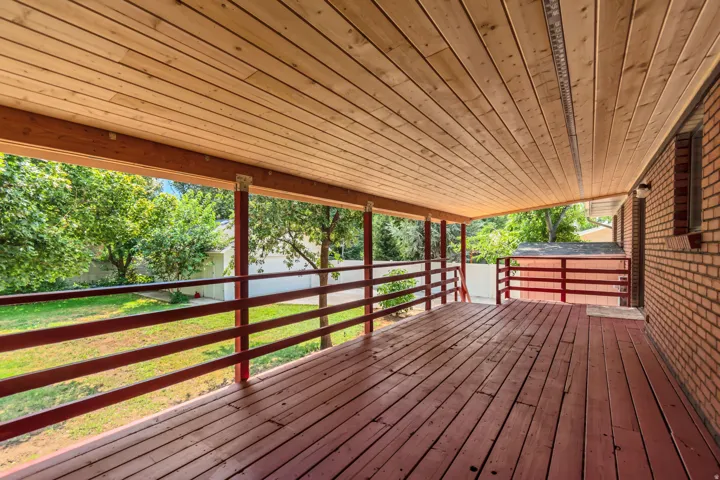 Expansive covered porch with wood plank ceiling and decking, metal railings, and open sightlines to mature landscaping