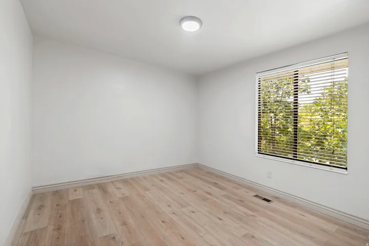 Neutral wall paint, wood-finish flooring, and a single window with blinds