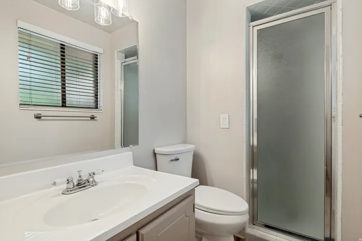 Vanity with integrated sink, chrome faucet, wall-mounted mirror, and frosted glass shower enclosure