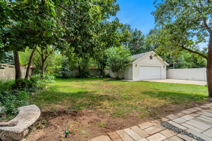 Expansive backyard oasis featuring mature trees providing natural shade, a manicured lawn, and a detached garage with driveway access