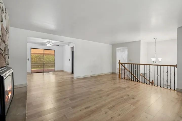 Spacious open loft featuring gleaming wood-finish flooring, abundant natural light from expansive glass doors, a gas fireplace with black surround, pendant lighting, metal railing details, and soaring ceilings with recessed lighting