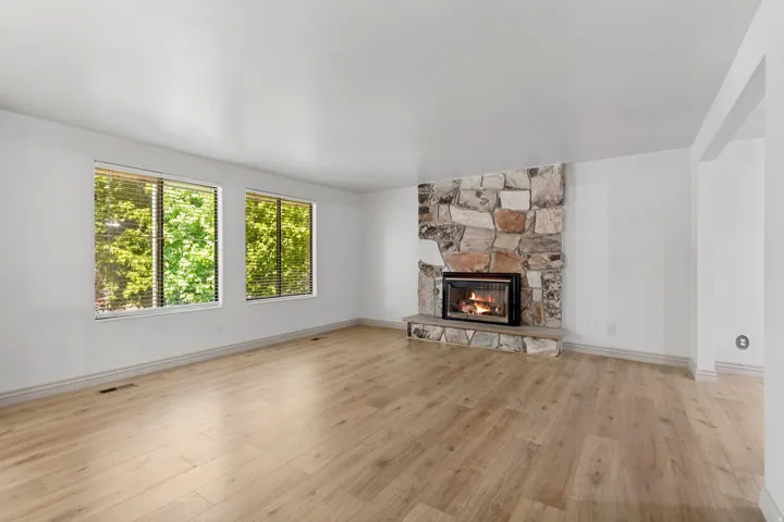 Stone-clad fireplace with hearth, two large windows, and light wood-finish flooring