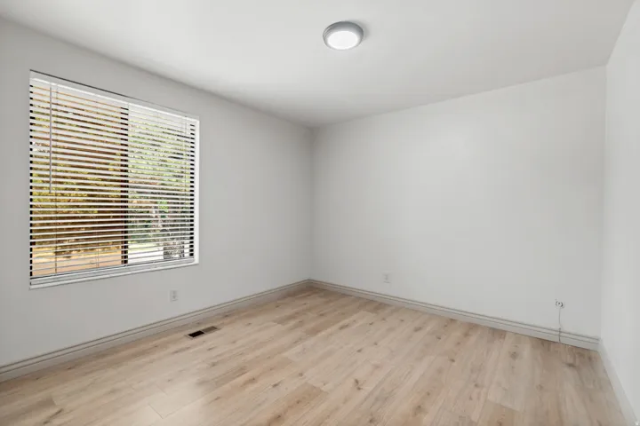 Wood-finish flooring, white walls, window with horizontal blinds, and a flush-mount ceiling light