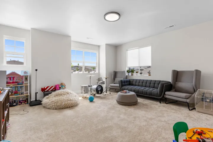 Spacious interior room with light neutral carpet, multiple windows providing natural illumination, recessed lighting, and crisp white walls