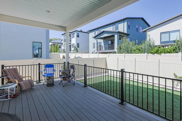 Covered deck featuring composite decking, black metal railings, and a fenced backyard with artificial turf
