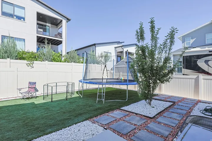 Landscaped backyard featuring artificial turf, a privacy fence, and a paver pathway with white and red stone accents
