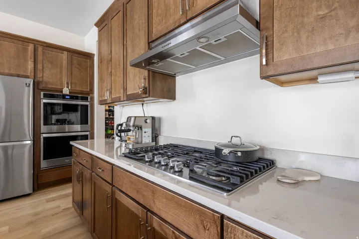Wood-finish flooring with a gas cooktop, stainless steel range hood, stainless steel double oven, and stainless steel refrigerator