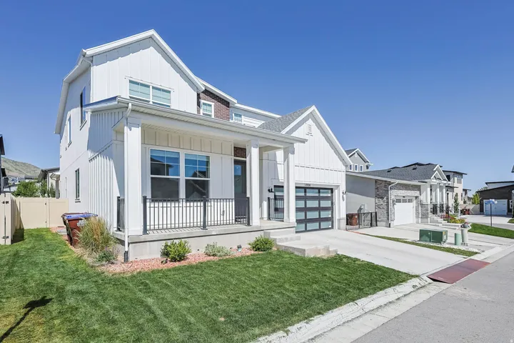 Modern residential exterior with white vertical siding, a covered entry porch, an integrated garage with a glass-paneled door, and a concrete driveway