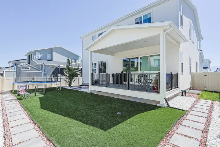 Covered patio with sliding glass door access, artificial turf lawn, privacy fencing, and stone paver pathways