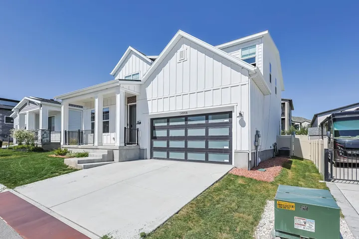 White board-and-batten siding with a covered front porch, a glass panel garage door, and a concrete driveway
