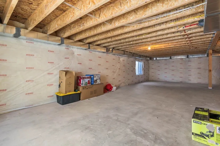 Unfinished basement with exposed ceiling joists, concrete flooring, and an egress window