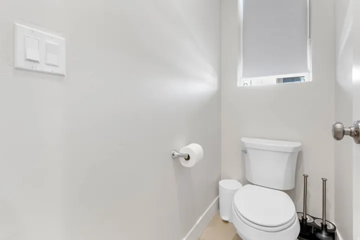White toilet with a window, light-colored flooring, and brushed nickel door hardware