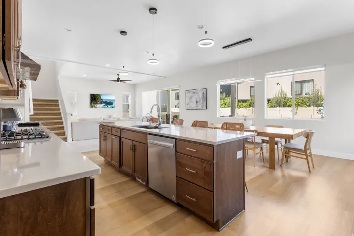 Open-concept kitchen and dining area featuring a large center island with wood cabinetry and stainless steel appliances, wide-plank wood-finish flooring, recessed and pendant lighting, and expansive windows with natural light throughout the space
