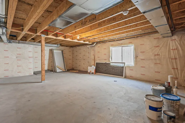Unfinished basement with exposed ceiling joists, concrete flooring, and a single window