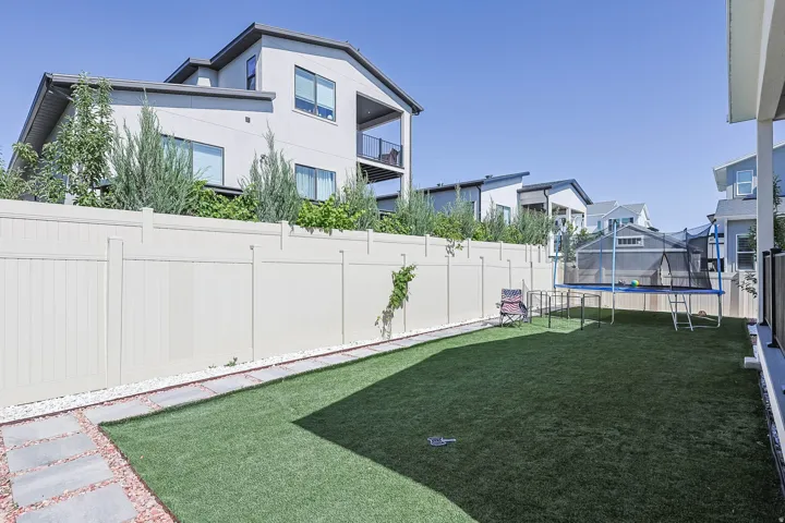 Expansive backyard with artificial turf, a white privacy fence, and a stone paver pathway