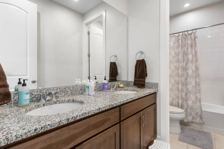 Dual vanity with granite countertop, integrated sinks, wood-finish cabinetry, and chrome fixtures