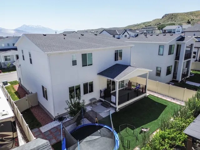 Modern two-story residence featuring a clean white exterior with multiple windows, a covered patio with pergola-style shade structure, professionally landscaped grounds with established lawn and mature plantings, and a fenced yard perimeter